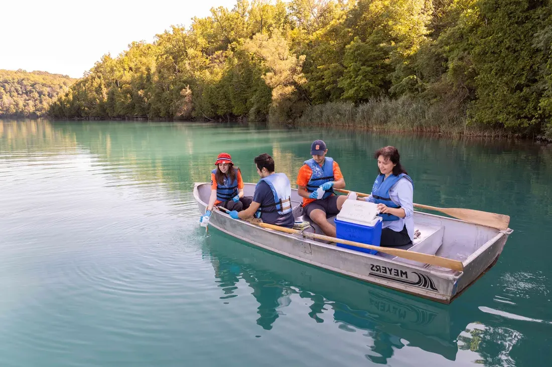 College of Arts and Science students on a boat at Green Lakes Park getting -water samplings out of the lake.